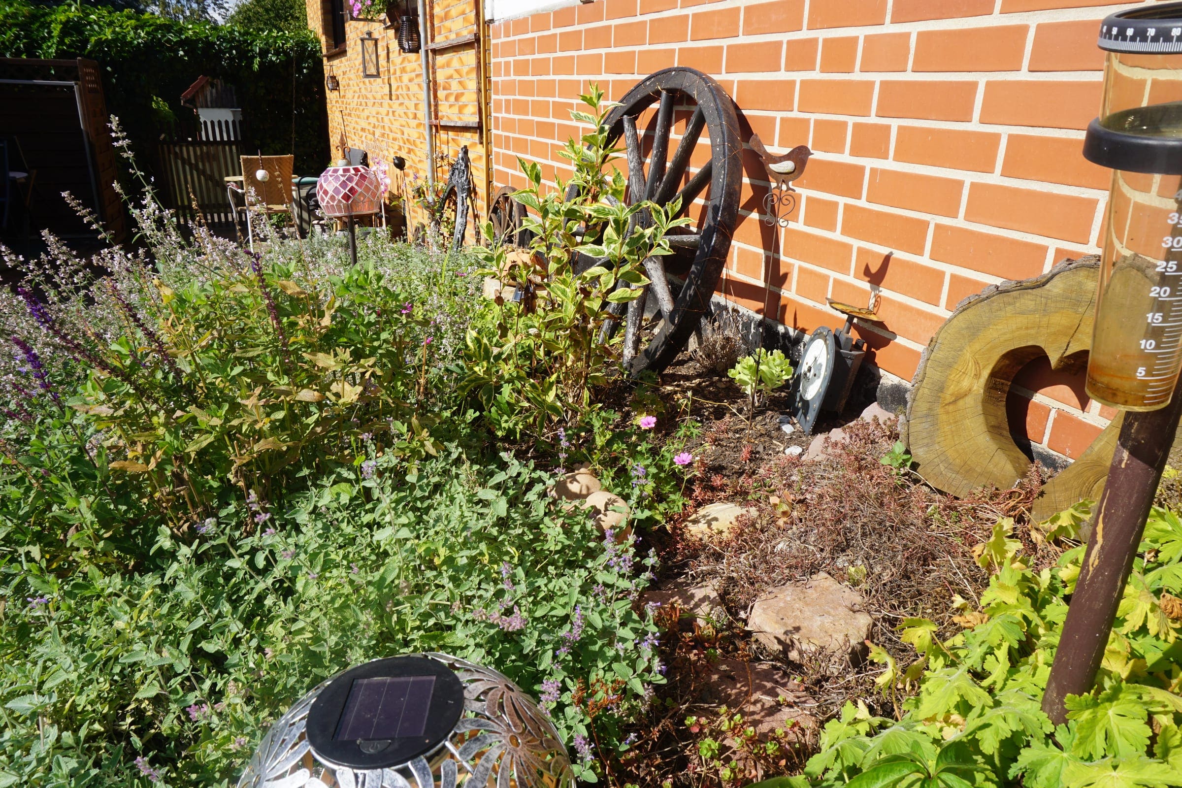 Staudenbeet mit Lavendel und altem Wagenrad vor einer Hausfassade